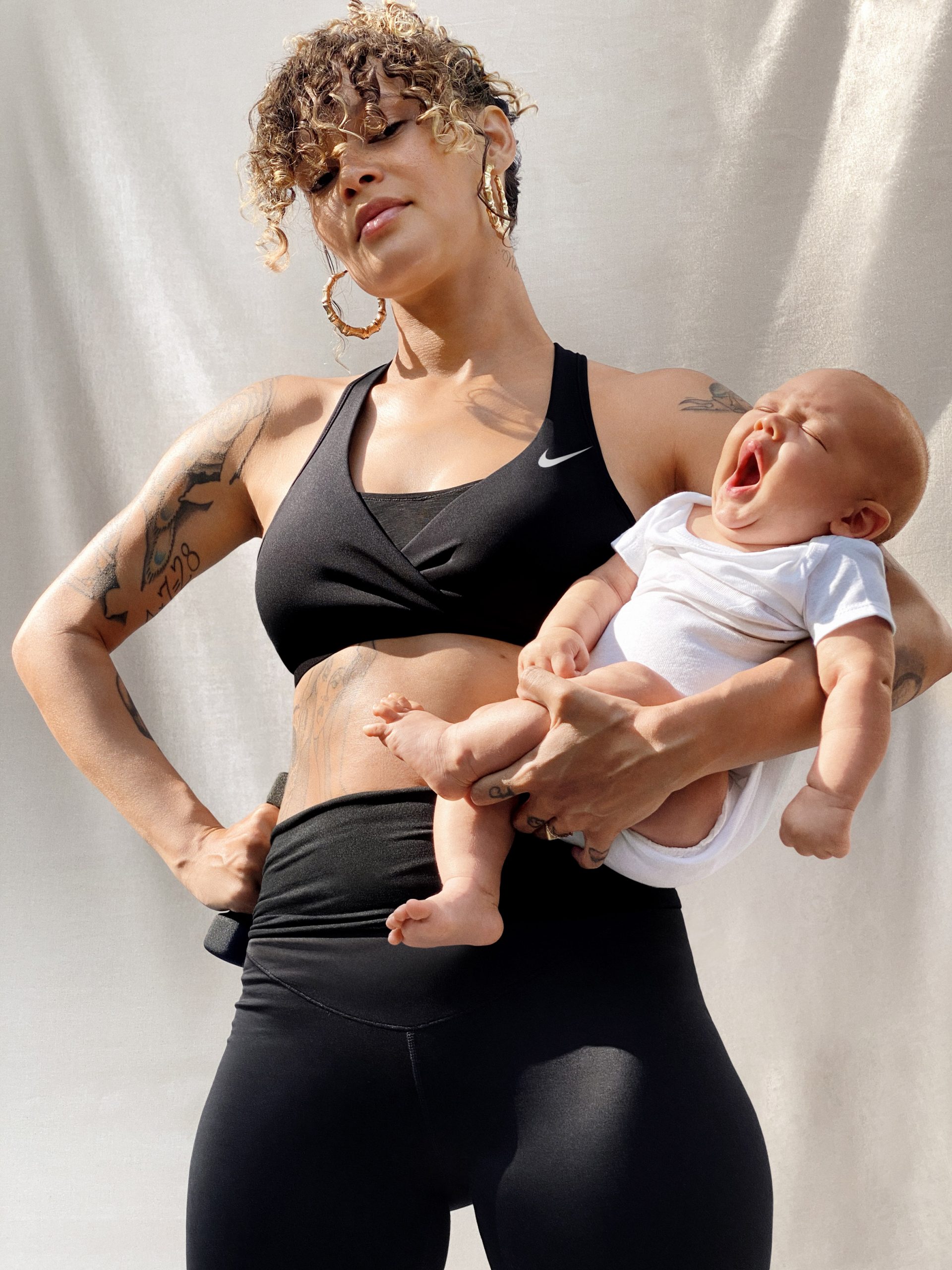 Mother laughing while holding her infant, wearing the Nike (M) Swoosh bra — the first Nike bra designed for both sport and nursing